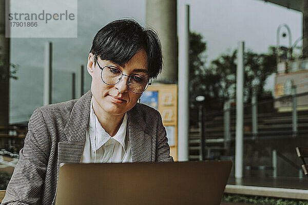 Geschäftsfrau mit Brille und Laptop sitzt im Straßencafé