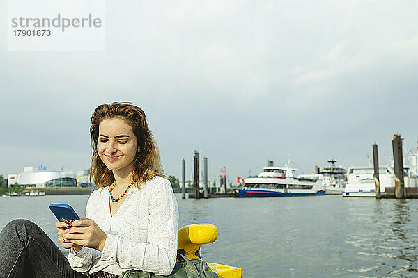 Lächelnde Frau mit Mobiltelefon im Hamburger Hafen  Deutschland