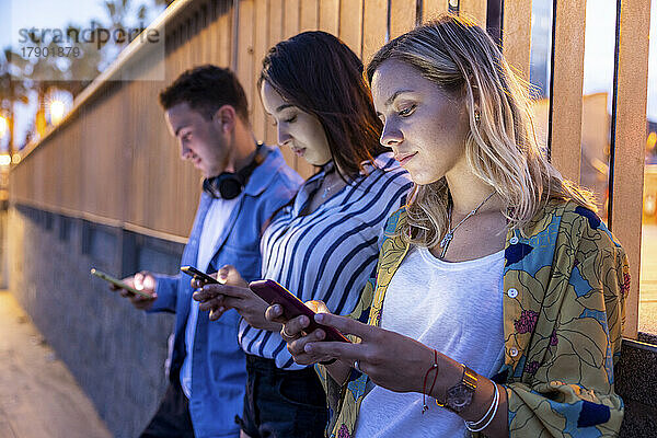 Junge Frauen und Männer surfen nachts vor dem Geländer mit Smartphones im Internet