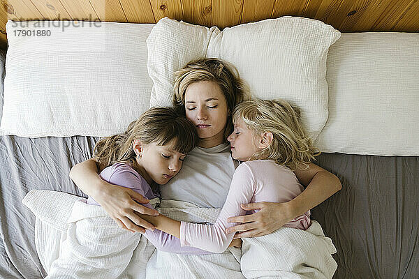 Mother with daughters sleeping in bed at home