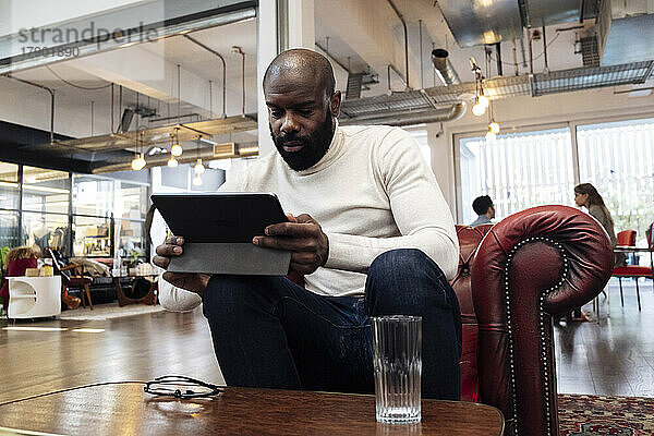 Selbstbewusster Geschäftsmann sitzt im Sessel und nutzt digitales Tablet