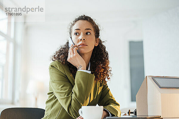 Geschäftsfrau sitzt am Schreibtisch im Büro und telefoniert mit ihrem Smartphone
