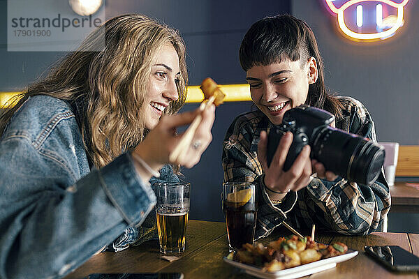 Lächelndes junges lesbisches Paar mit Kamera  das am Tisch im Restaurant sitzt