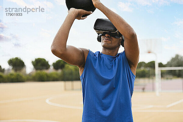 Junger Mann mit VR-Headset wirft Basketball auf Sportplatz