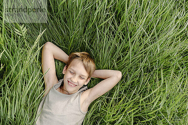 Glücklicher Junge mit geschlossenen Augen  der sich auf Gras legt