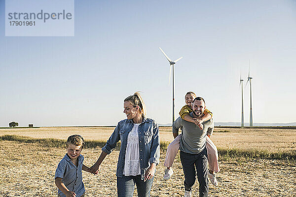 Selbstbewusste Familie geht Händchen haltend durch den Windpark