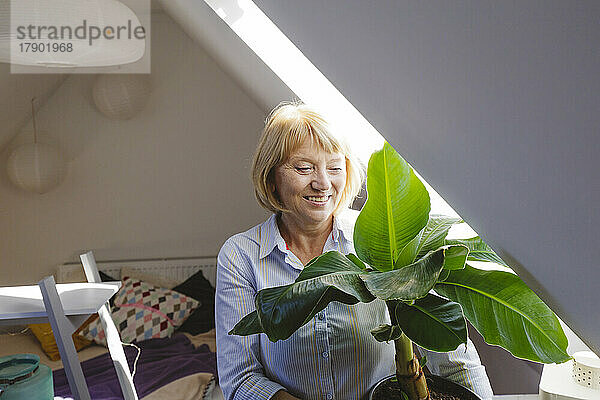 Glückliche ältere Frau mit Bananenpflanze sitzt im Schlafzimmer