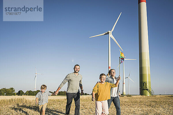 Optimistische Familie geht im Windpark spazieren. Tochter trägt buntes Windrad