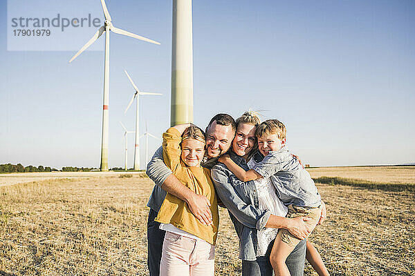 Glückliche Familie steht im Windpark und umarmt Kinder