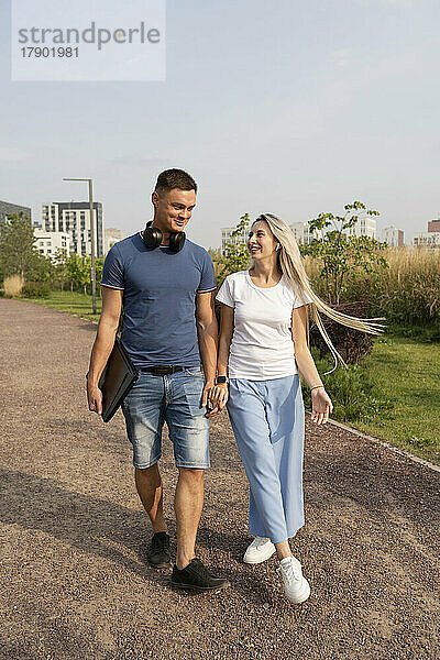 Glücklicher Freund und Freundin gehen gemeinsam Händchen haltend im Park spazieren