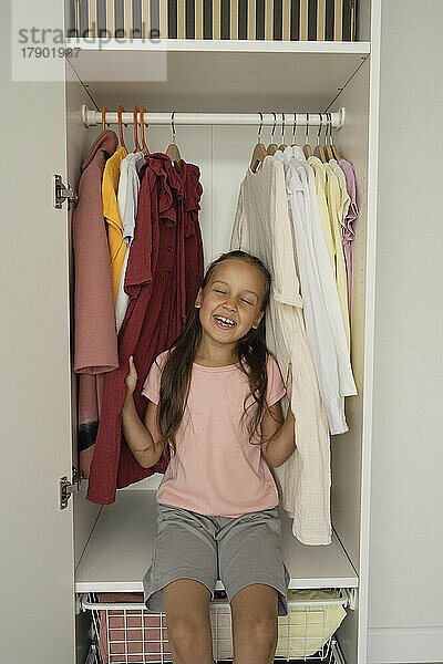 Happy girl with eyes closed sitting by clothes in closet