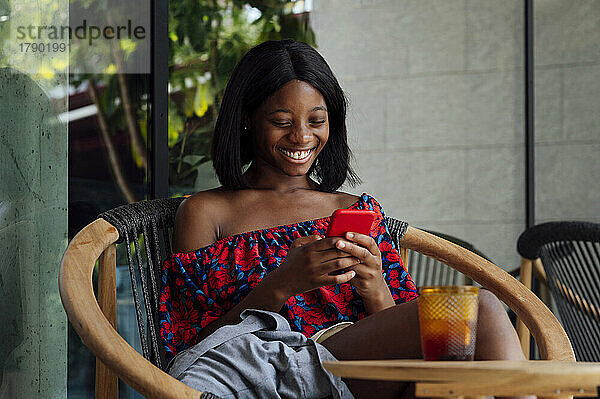 Glückliche Frau  die im Straßencafé Textnachrichten per Smartphone sendet