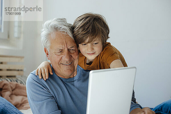 Lächelnder älterer Mann  der zu Hause ein Selfie mit seinem Enkel über einen Tablet-PC macht