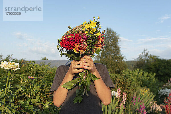 Junge hält an einem sonnigen Tag einen Blumenstrauß übers Gesicht