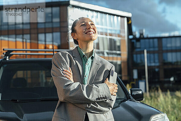 Glückliche Geschäftsfrau  die an einem sonnigen Tag vor dem Auto steht