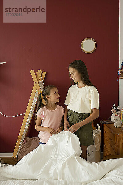 Girls making bed together in children's room at home