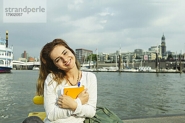 Glückliche schöne Frau mit Tagebuch sitzt im Hamburger Hafen  Deutschland