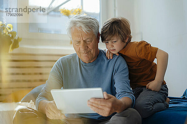 Älterer Mann teilt Tablet-PC mit Enkel im heimischen Wohnzimmer