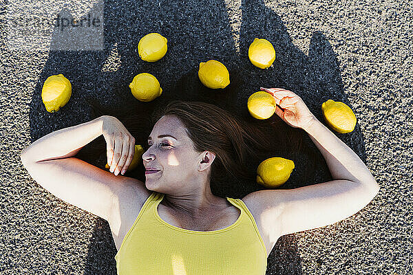 Smiling woman lying down on asphalt with lemons