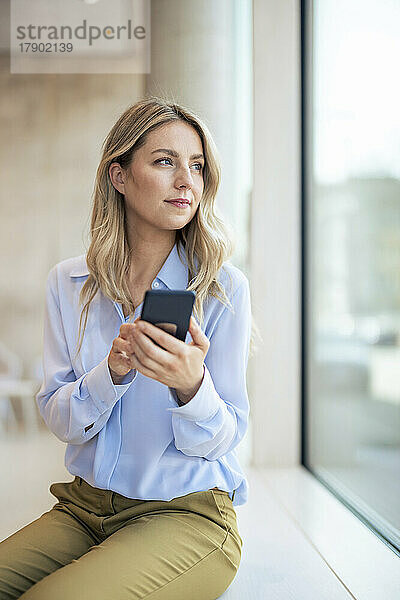 Nachdenkliche Geschäftsfrau mit Smartphone im Büro