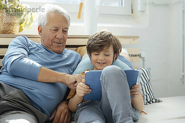 Lächelnder Junge teilt zu Hause Tablet-PC mit Großvater