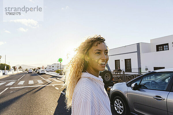 Happy young woman crossing street on sunny day