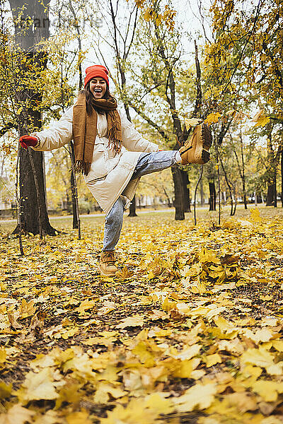 Glückliche junge Frau kickt Herbstblätter im Park