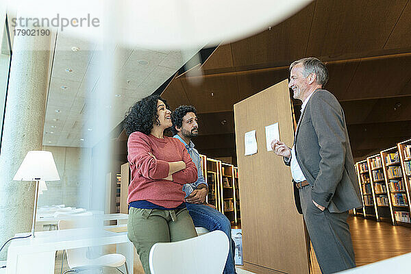 Lächelnder Mann mit der Hand in der Tasche im Gespräch mit Kollegen in der Universitätsbibliothek