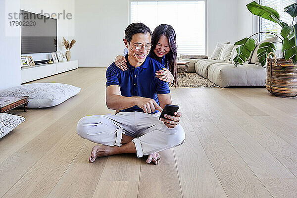 Glücklicher Mann teilt Smartphone mit Frau im Wohnzimmer zu Hause
