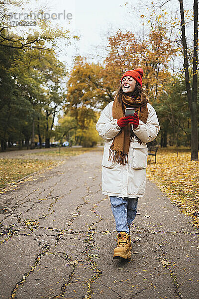 Glückliche junge Frau mit Smartphone läuft auf Fußweg im Park