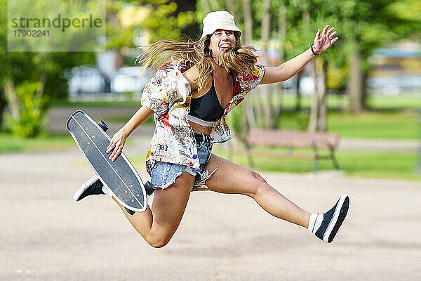 Sorglose Frau mit Skateboard springt im Park