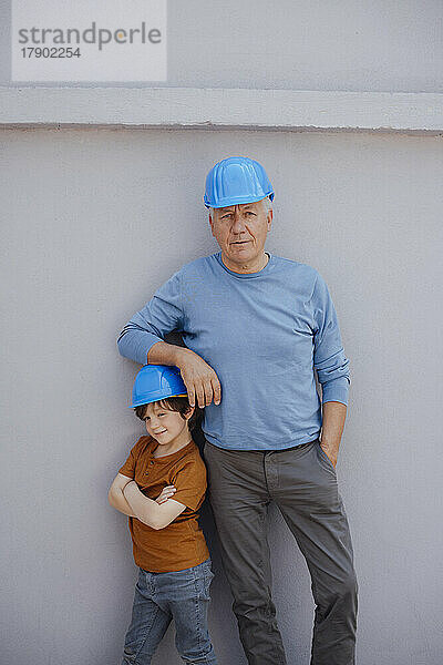 Selbstbewusster älterer Mann mit Helm und Enkel vor der Wand