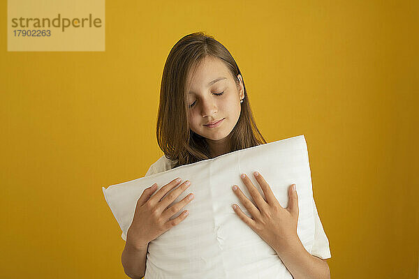 Girl with eyes closed holding white pillow against yellow background