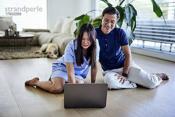 Lächelnder Freiberufler benutzt Laptop von Mann im Wohnzimmer zu Hause
