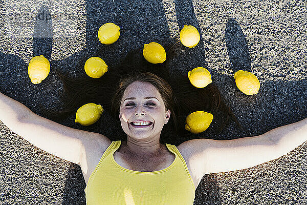 Happy woman with arms outstretched lying down on road amidst lemons
