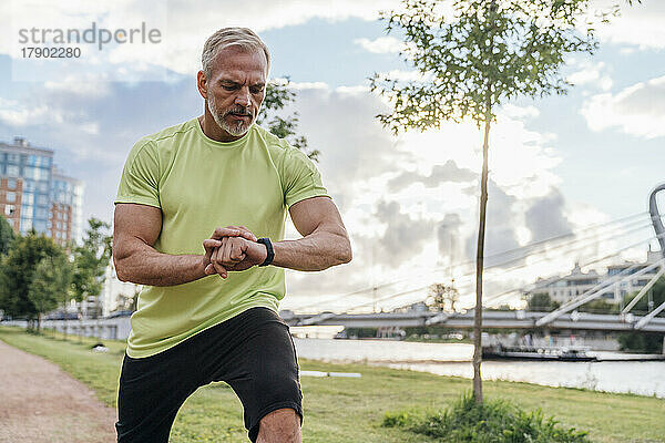 Mann überprüft Fitness-Tracker beim Stretching im Park