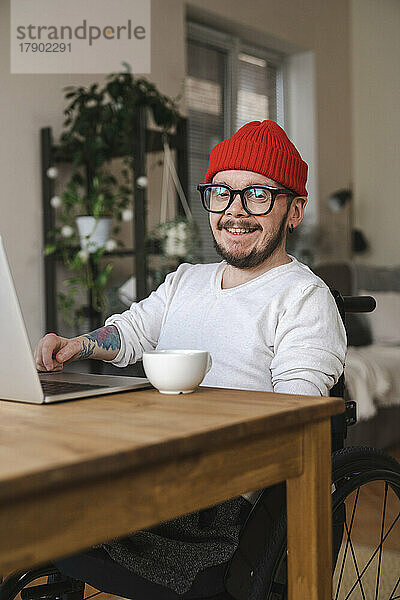 Lächelnder Mann im Rollstuhl mit Laptop zu Hause