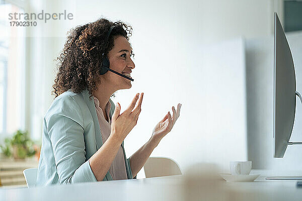 Lächelnde Geschäftsfrau spricht über Headset und gestikuliert im Büro