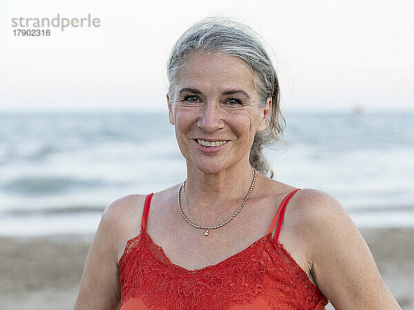 Glückliche ältere Frau im Ruhestand mit grauen Haaren am Strand