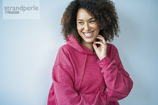 Happy woman wearing hooded shirt in front of white wall