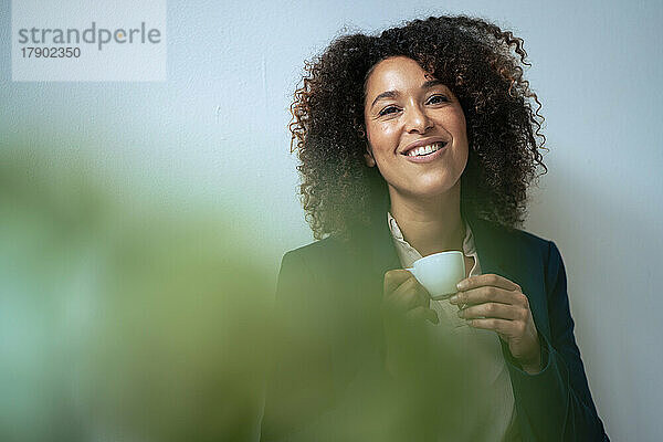 Lächelnde Geschäftsfrau beim Kaffee vor der Wand