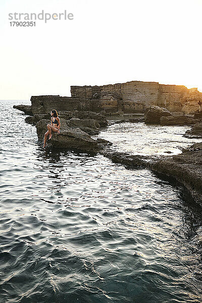 Woman relaxing on rock by sea