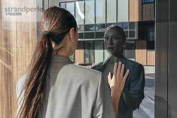 Geschäftsfrau blickt auf Reflexion an Glastür