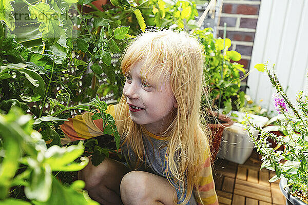 Glückliches Mädchen  das neben einer Pflanze auf dem Balkon sitzt