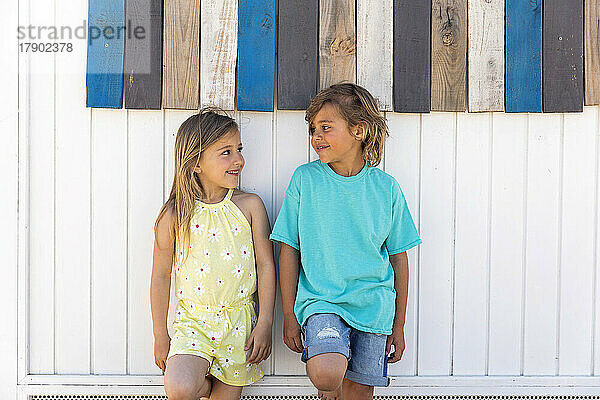 Smiling cute girl with boy leaning on wooden wall