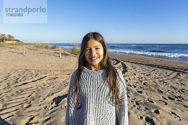Glückliches Mädchen im Pullover  das am Strand steht