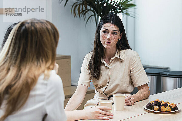 Junge Geschäftsfrau diskutiert mit einem Kollegen  der in der Cafeteria sitzt