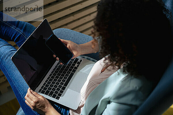 Businesswoman with laptop using smart phone at workplace