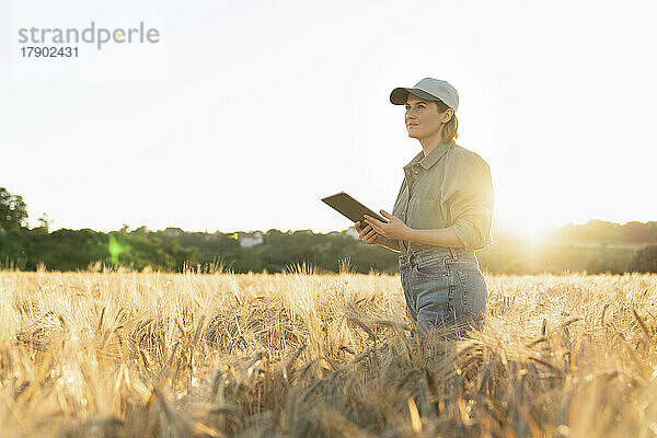 Frau steht bei Sonnenuntergang mit digitalem Tablet im Feld