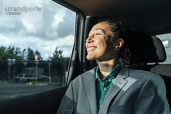 Glückliche Geschäftsfrau sitzt im Auto und schaut durch das Fenster
